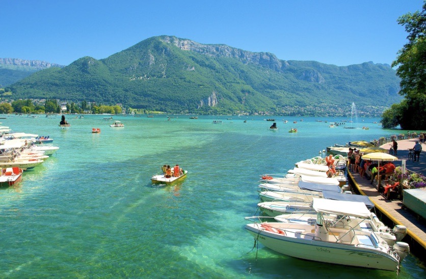 The shoreline of Lake Annecy with boats moored on turquoise water